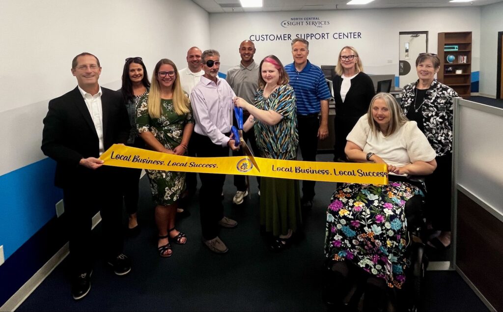 NCSS employees and community members stand behind a large ribbon. Two employees are holding large scissors.